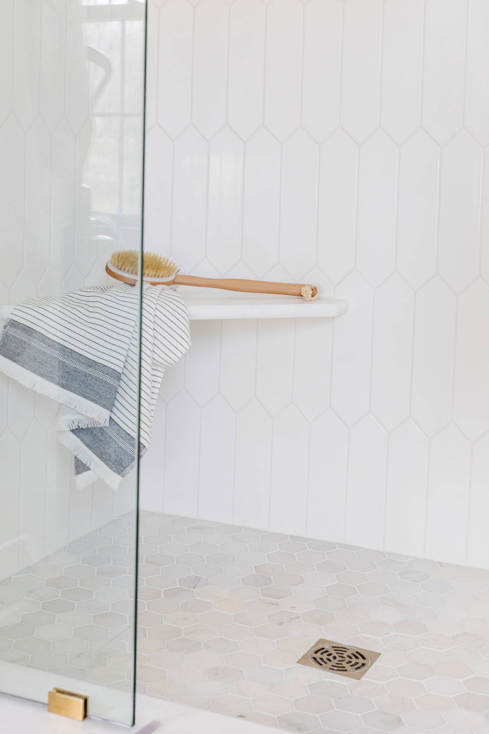 Tiled bathroom shower with white picket wall tile and marble hex mosaic flooring