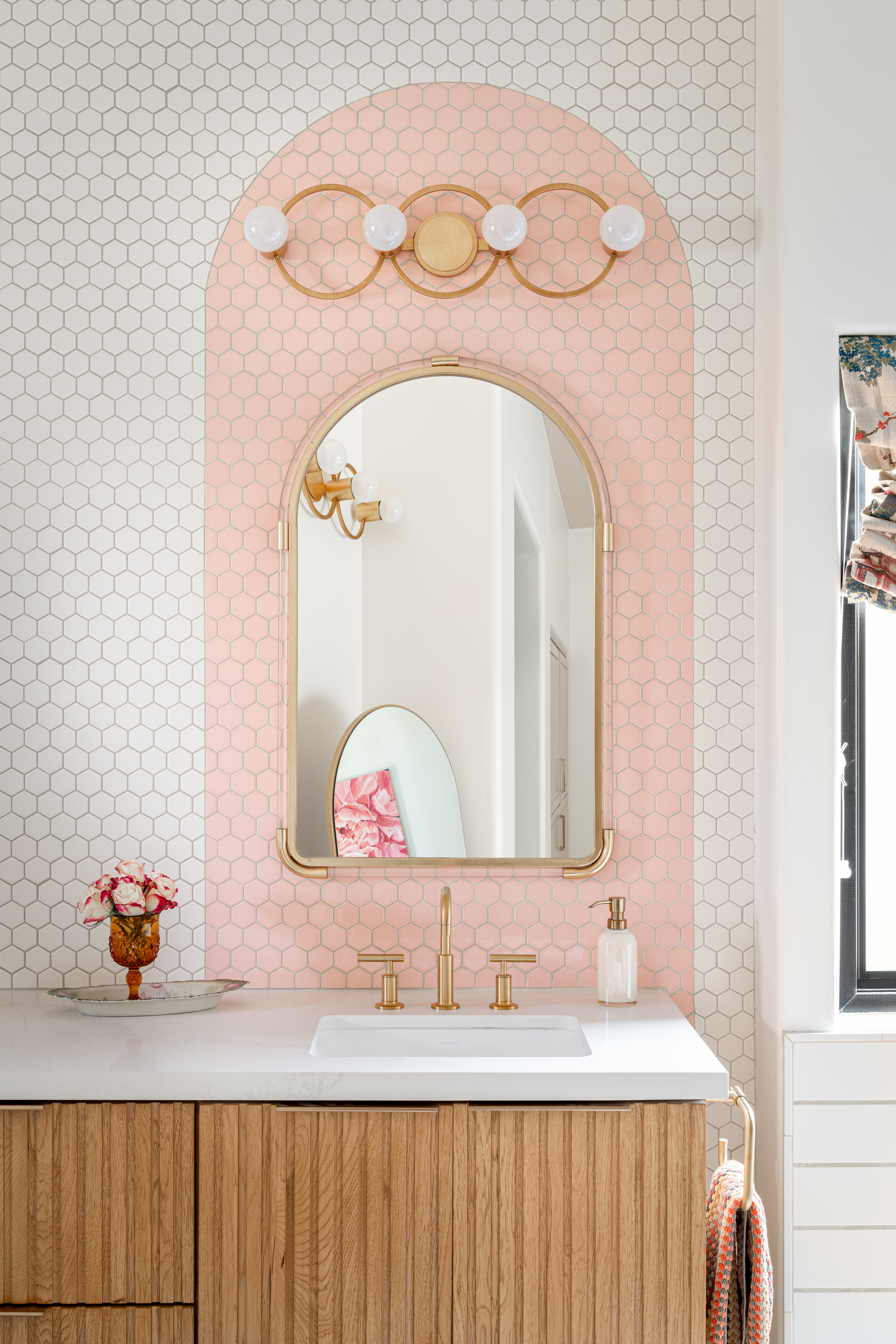 Art deco bathroom with fluted wood vanity and pink tiled arches above sink