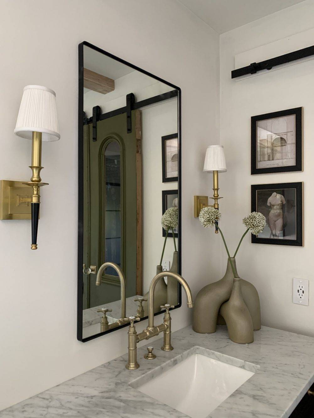 Detail shot of marble bathroom sink and black mirror with gold wall sconces