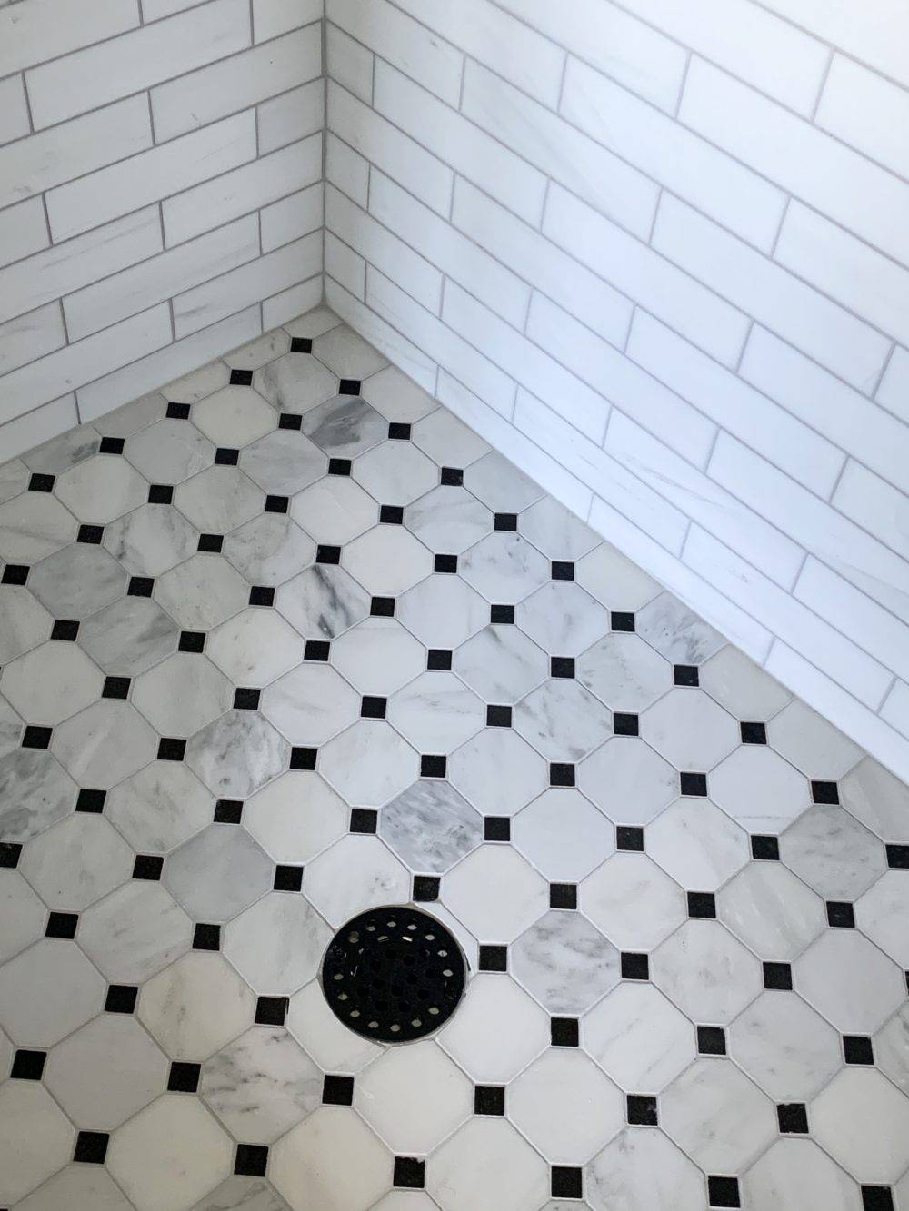 Black and white octagon polished marble mosaic on shower floor with white subway tile shower walls