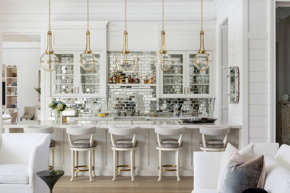 Long white bar with hanging gold light fixtures featuring Antique Mirror Bevel tile. 
