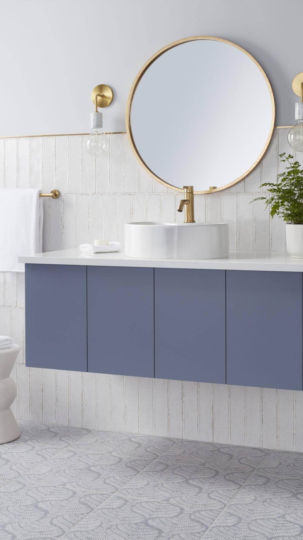Bathroom with blue patterned floor tile and white handmade-look wall tile with gold trim and blue vanity.
