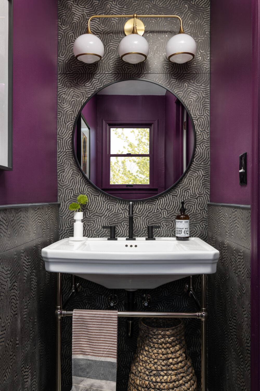 Dark purple and black and gold tile sink backsplash. White sink and circular mirror.