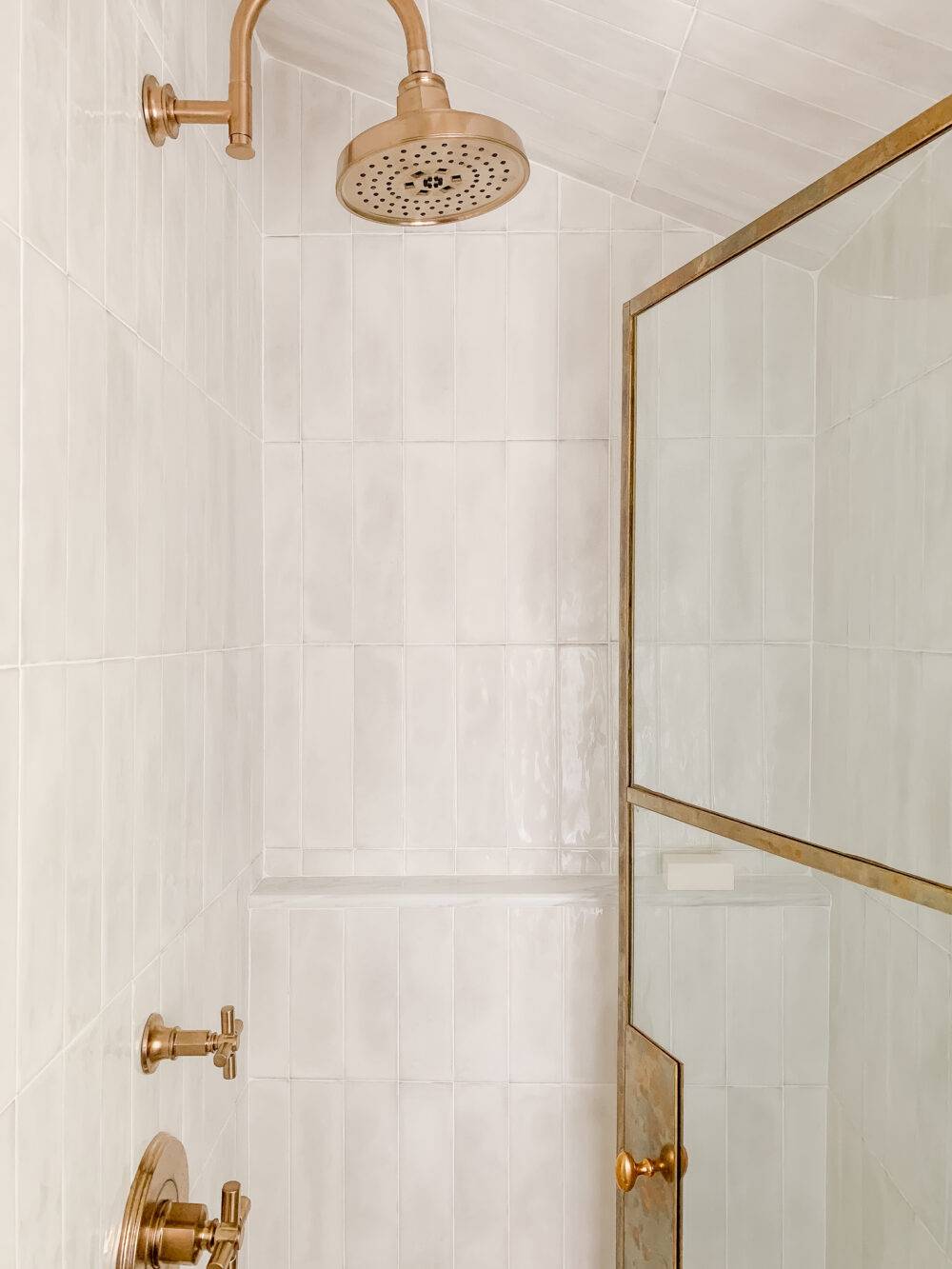 Shower with white handmade-look subway tile and brass fixtures. 