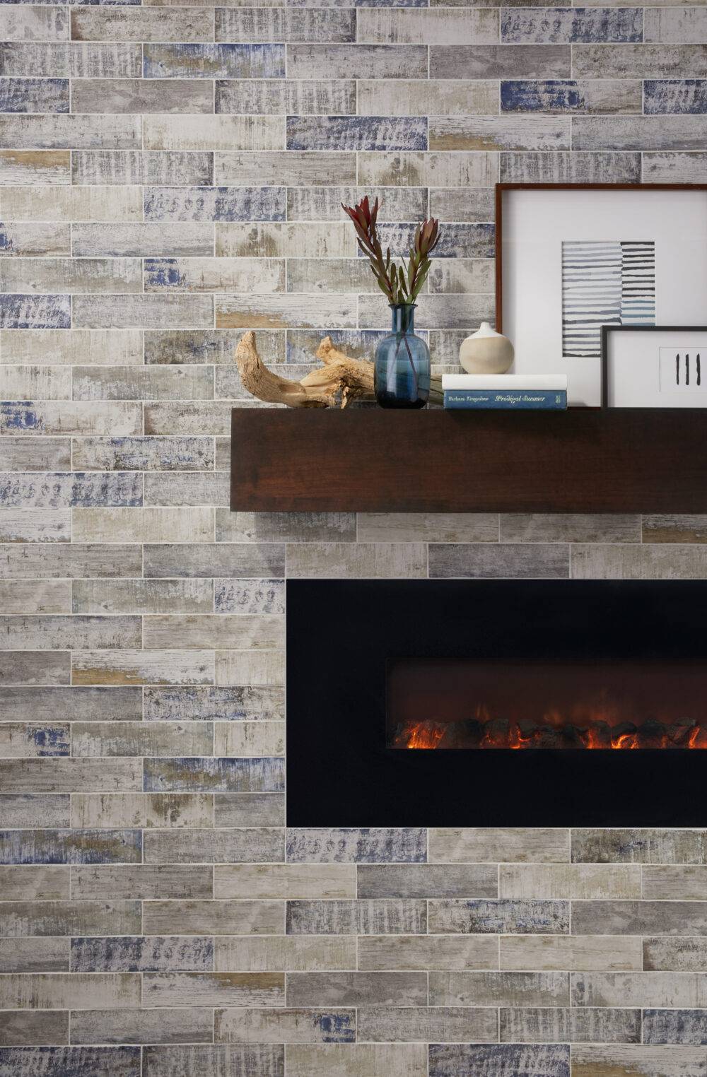 Fireplace surround with the rustic look of weathered wood in a ceramic subway tile set in a horizontal brick pattern. Mantal is a large floating pice of warner toned wood and fire box is matte black.  