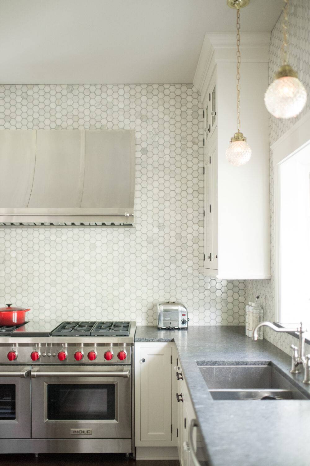 A kitchen with white cabinets and small hexagon-shaped marble backsplash. 