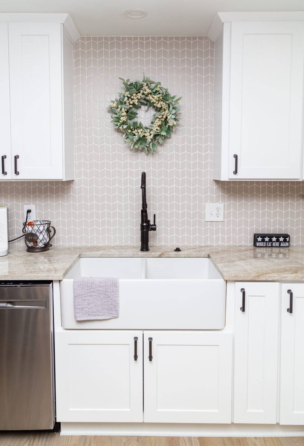 A kitchen with white cabinets and pale a grey colored leaf-shaped mosaic backsplash. 