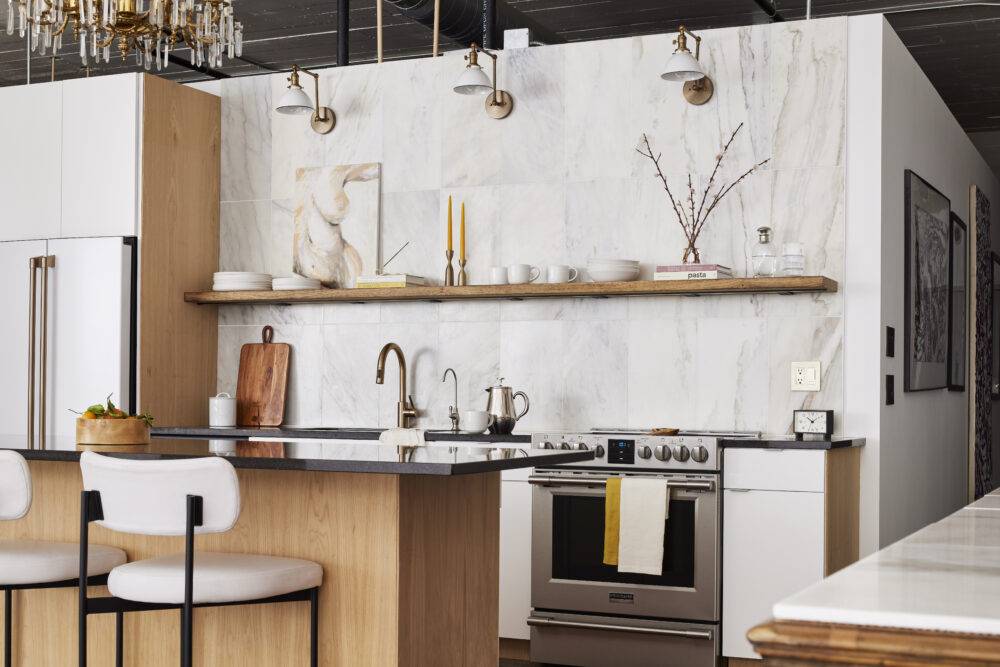 A loft kitchen with white cabinets and a large-format marble tiled wall. 