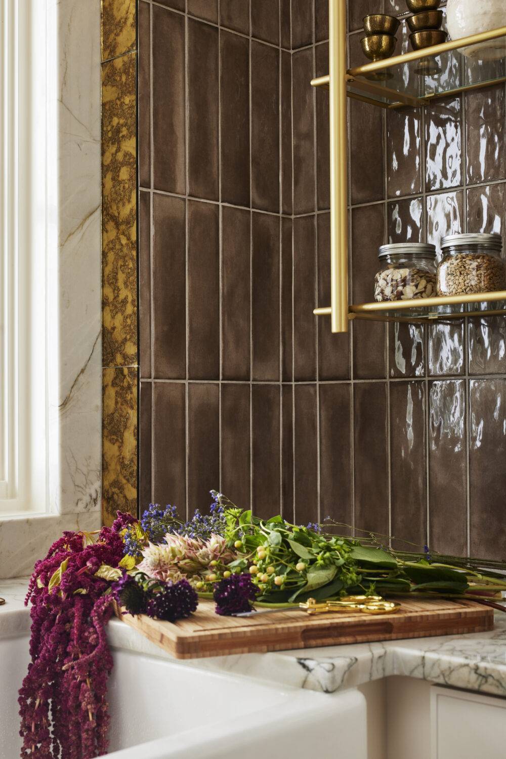 Close-up shot of the pantry counter with bouquet of flowers on the counter and brown handmade-look tile and gold patina mirrored tile trim. 