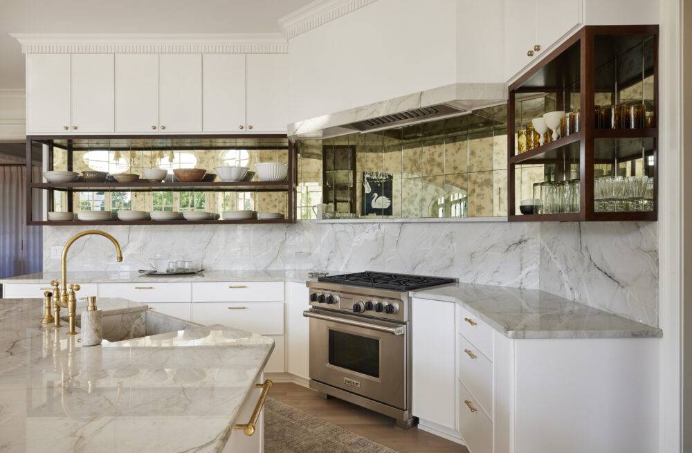 Kitchen with marble counters and backsplash and mirrored patina tile between the backsplash and cabinets.
