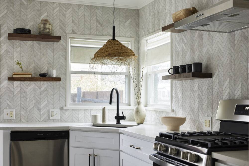 A kitchen with white cabinets and marble chevron patterned tile with grey veining. 