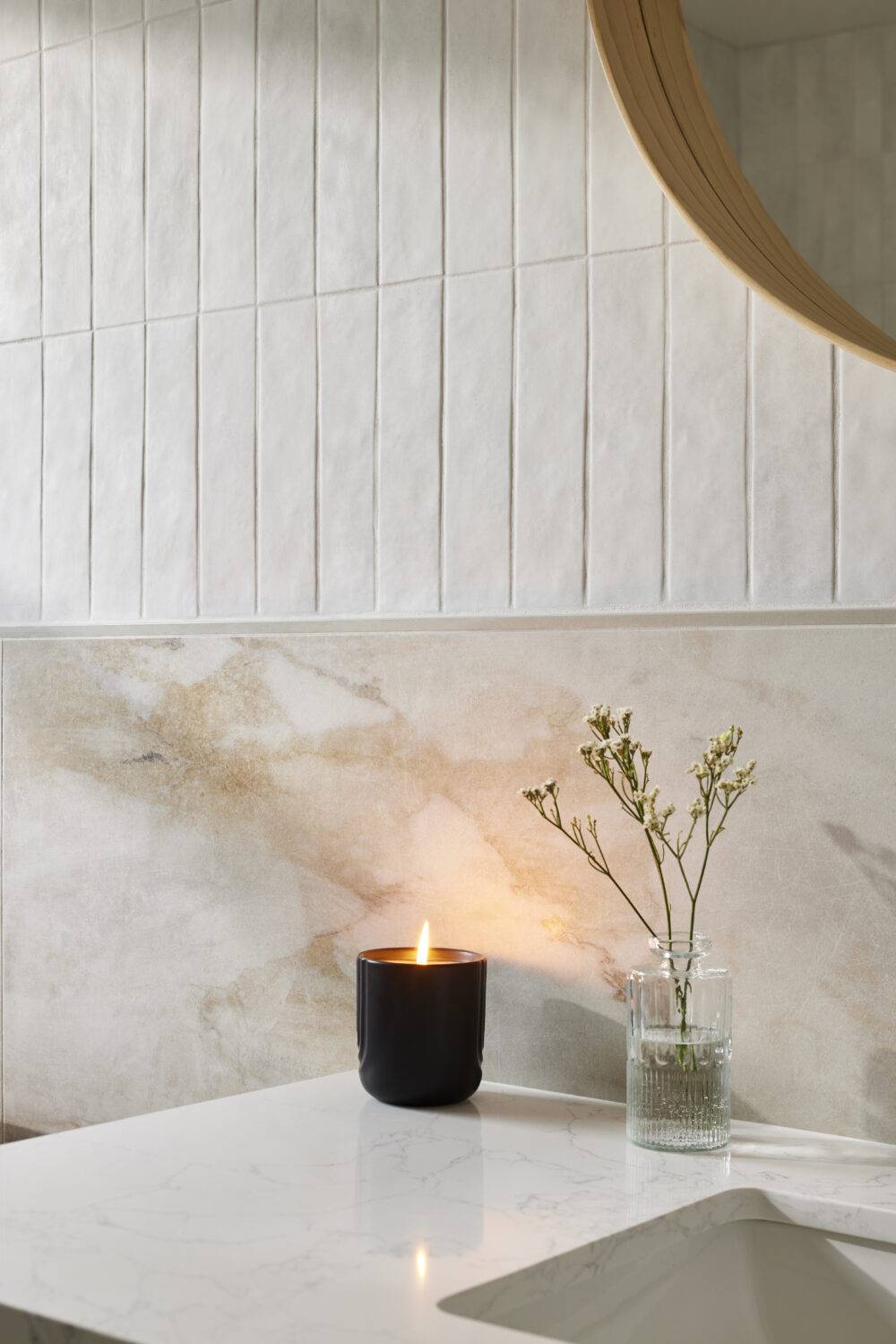White wall with marble-look and handmade-look tile and sink with a candle and small plant.