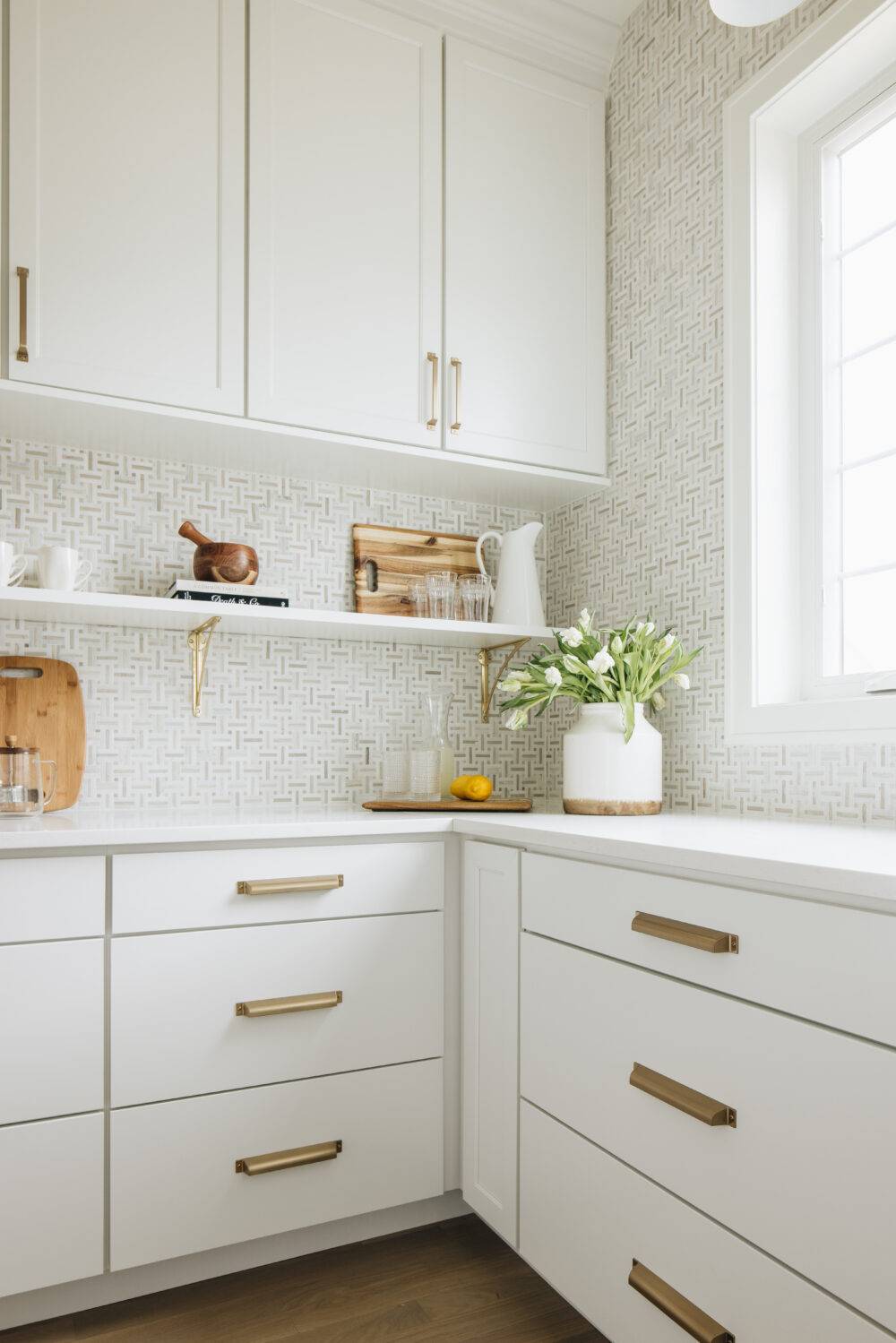 A kitchen with white cabinets and white and beige marble basketweave mosaic backsplash. 