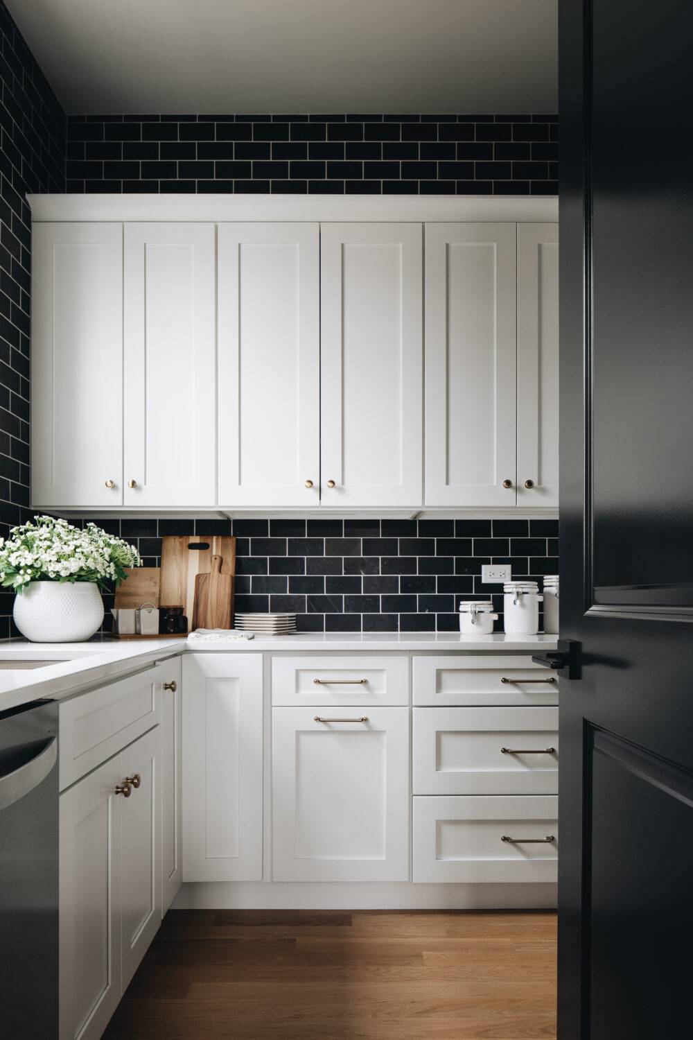 A kitchen with white cabinets and a black subway tile backsplash. 