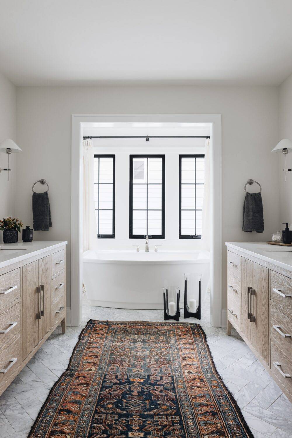 Luxurious white bathroom with white marble floor tiles in herringbone pattern and wooden cabinets. 