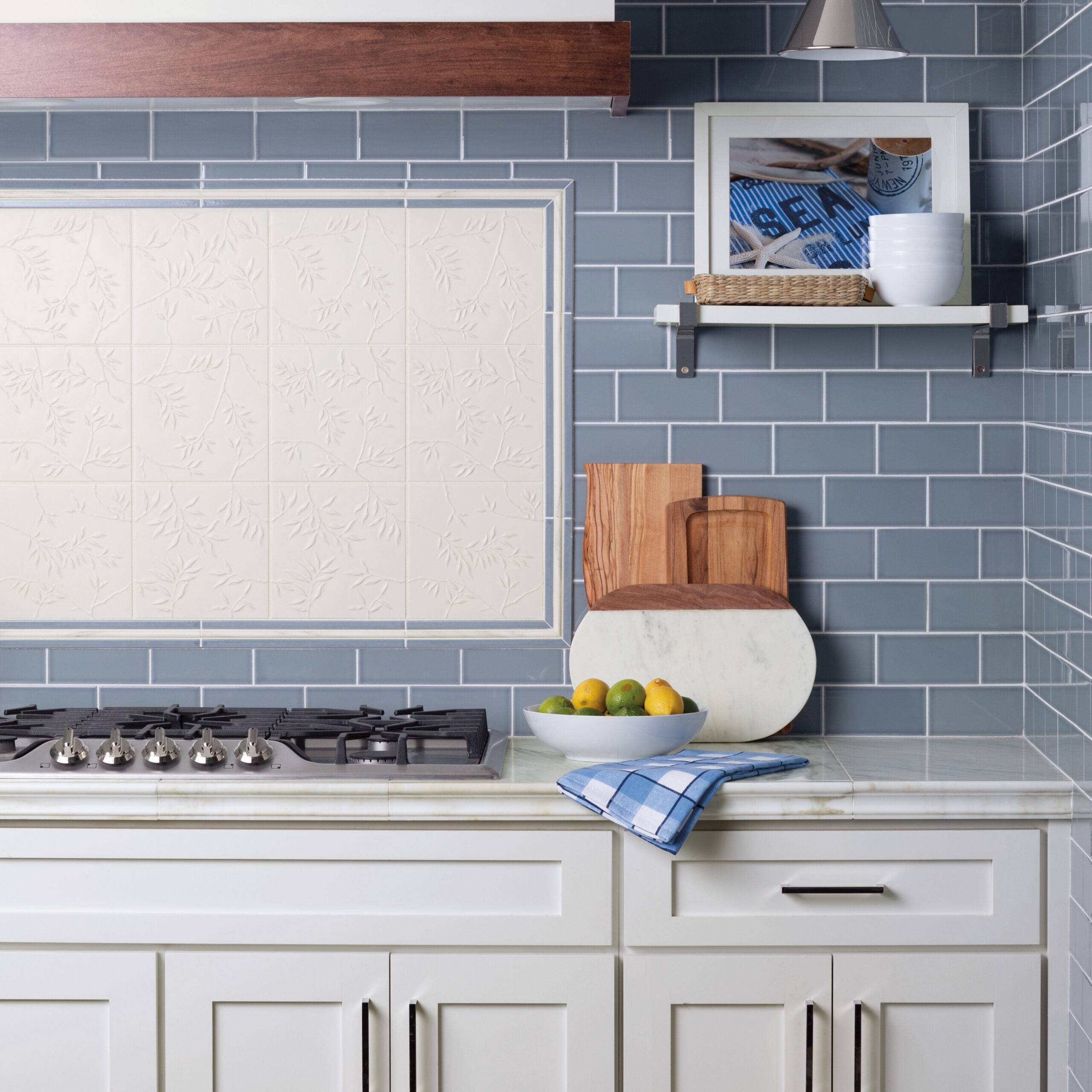 Marble counter top with blue ceramic tile backsplash with framed accent tile above range top.