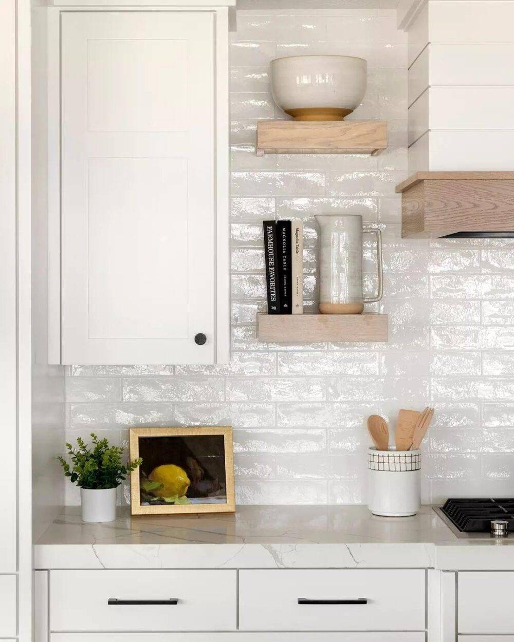 White handmade-look subway tile with white kitchen cabinets and small light wood shelves. 