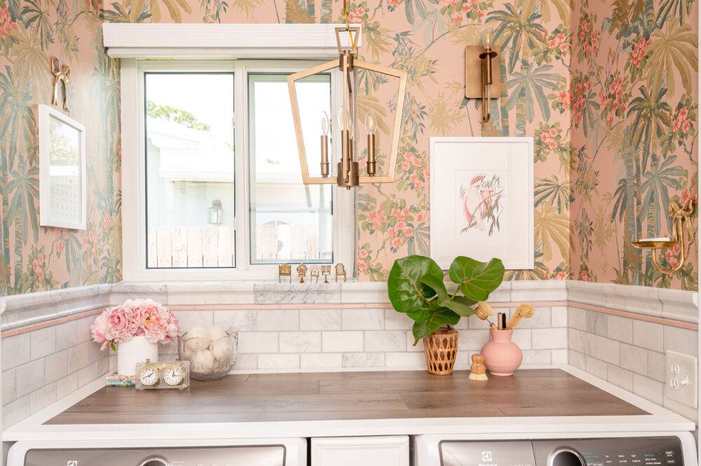 Laundry room with pink floral wallpaper and marble tile wall with pink pencil trim. 