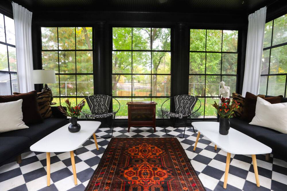 Four seasons porch with black-and-white checkerboard tile floor, black and white furniture and red rug.  