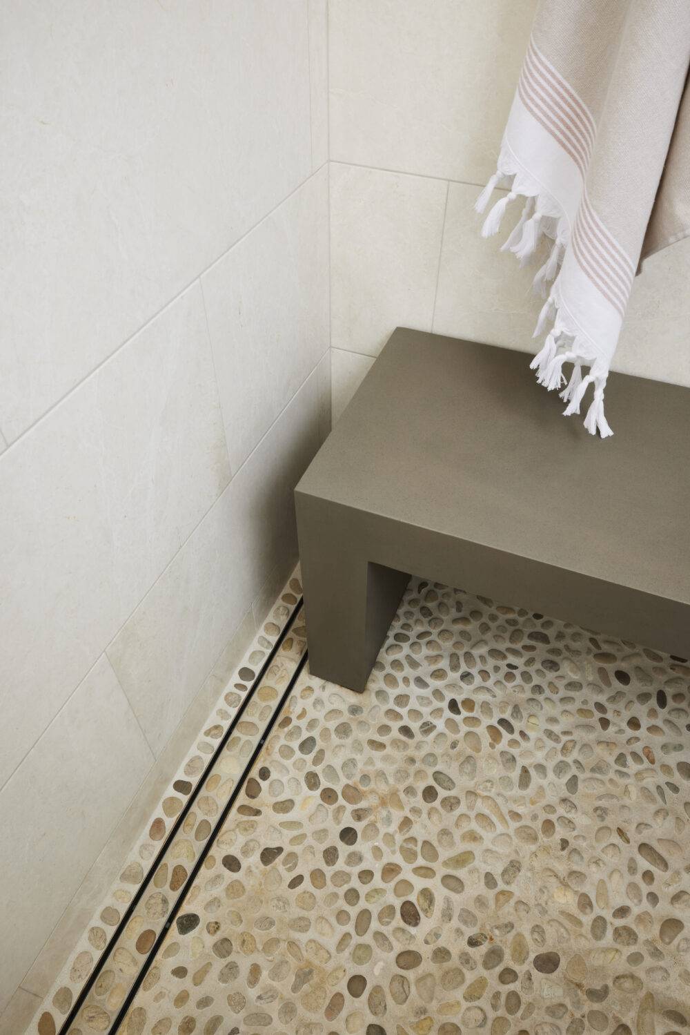 Corner shot of a shower with grey bench and pebble tile floor.