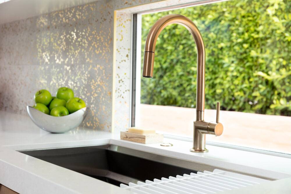 Gold kitchen faucet with white with gold speckled tile backsplash. 