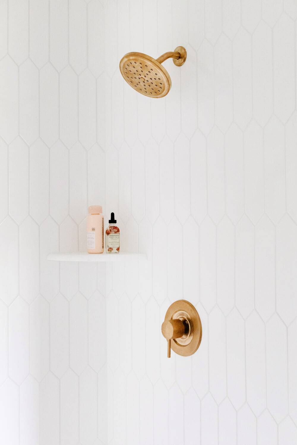 White picket-shaped tiled shower with white corner shelf. 