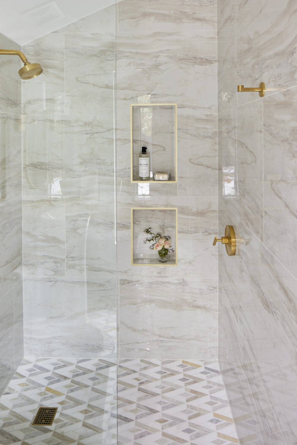 Shower with marble tile, gold fixtures and two small niches.