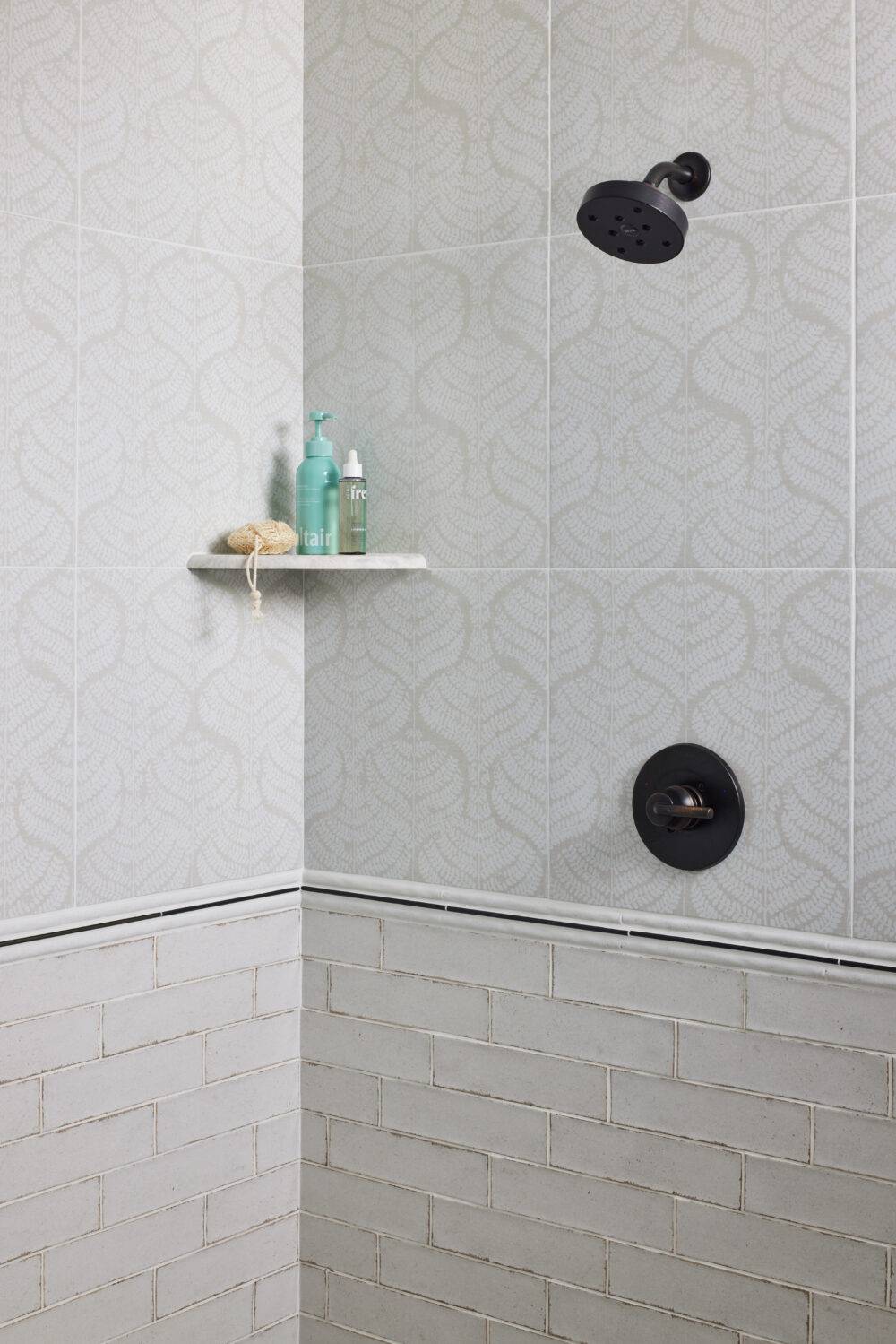 This shower features cream and white colored fern patterned tile and white handmade-look subway tile with corner shelf and trim tile. 