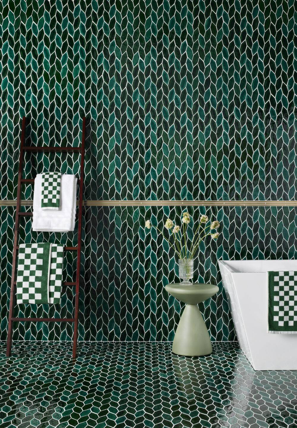 Green-leaf wall and floor tile with tub, towels and small green accent table with flowers.
