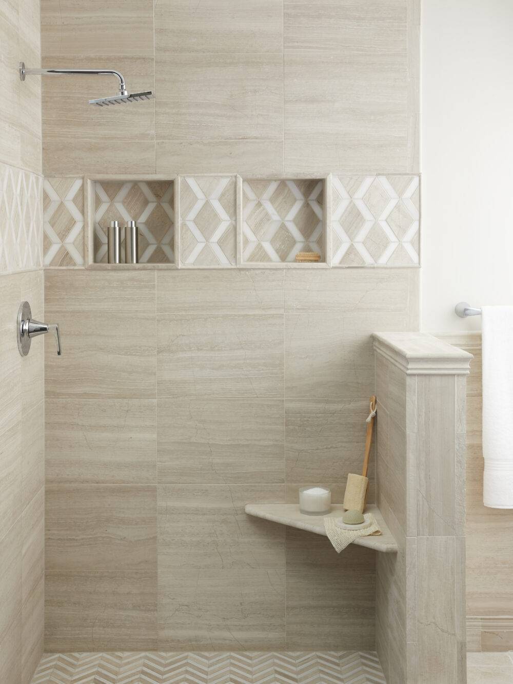 Walk in shower in bathroom area tiled with a vein cut limestone of taupe and grey coloration in several sizes and mosaics alike.  Mosaics are mixed with a white marble. Shower seat is same material. Fixtures are a polished chrome.