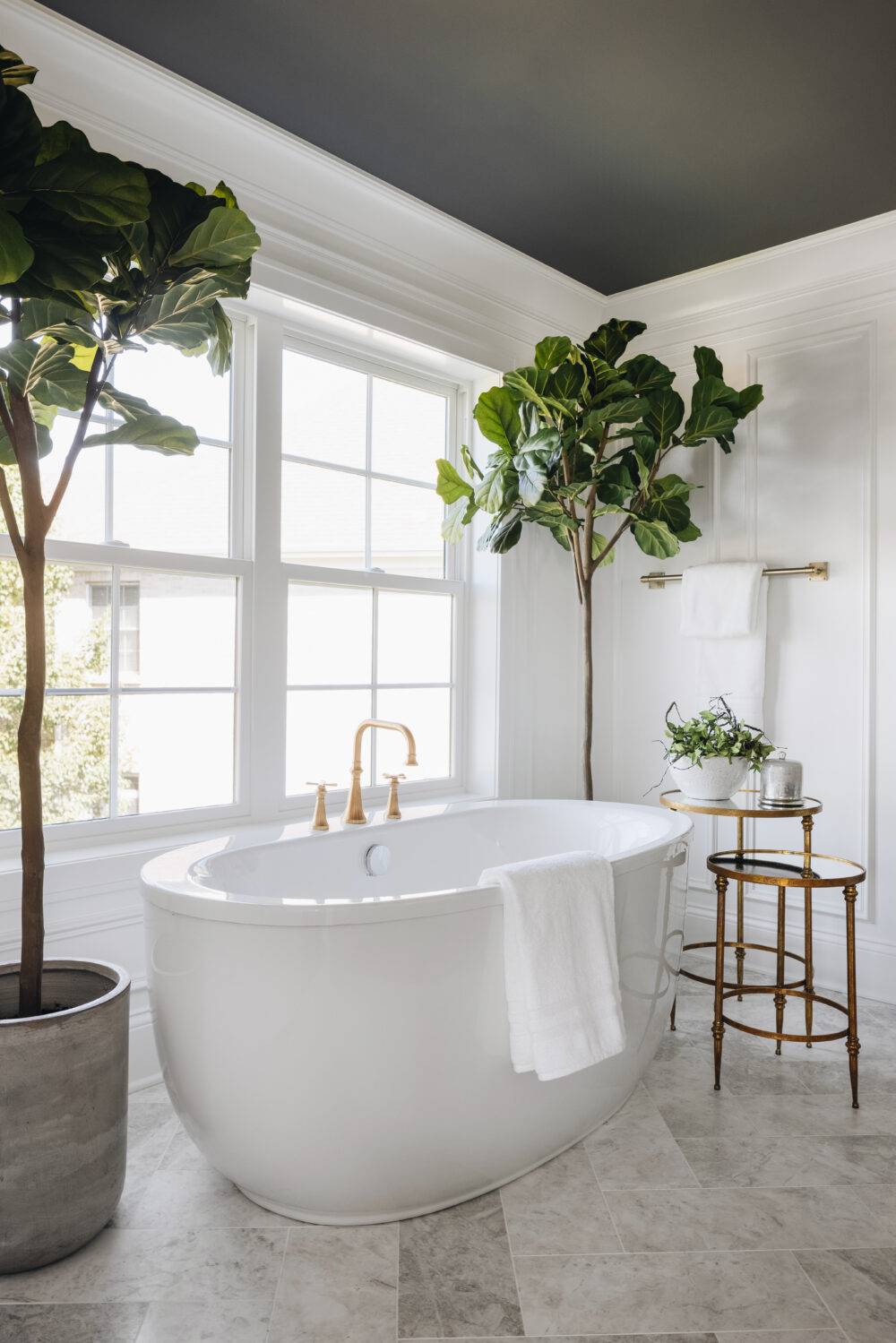 This is a white bathroom with white/grey marble floor and two small trees. 