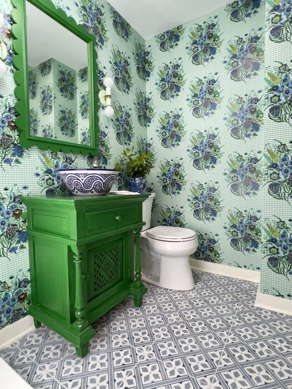 This green and blue bathroom features blue floral patterned floor tile and bold floral wallpaper. 