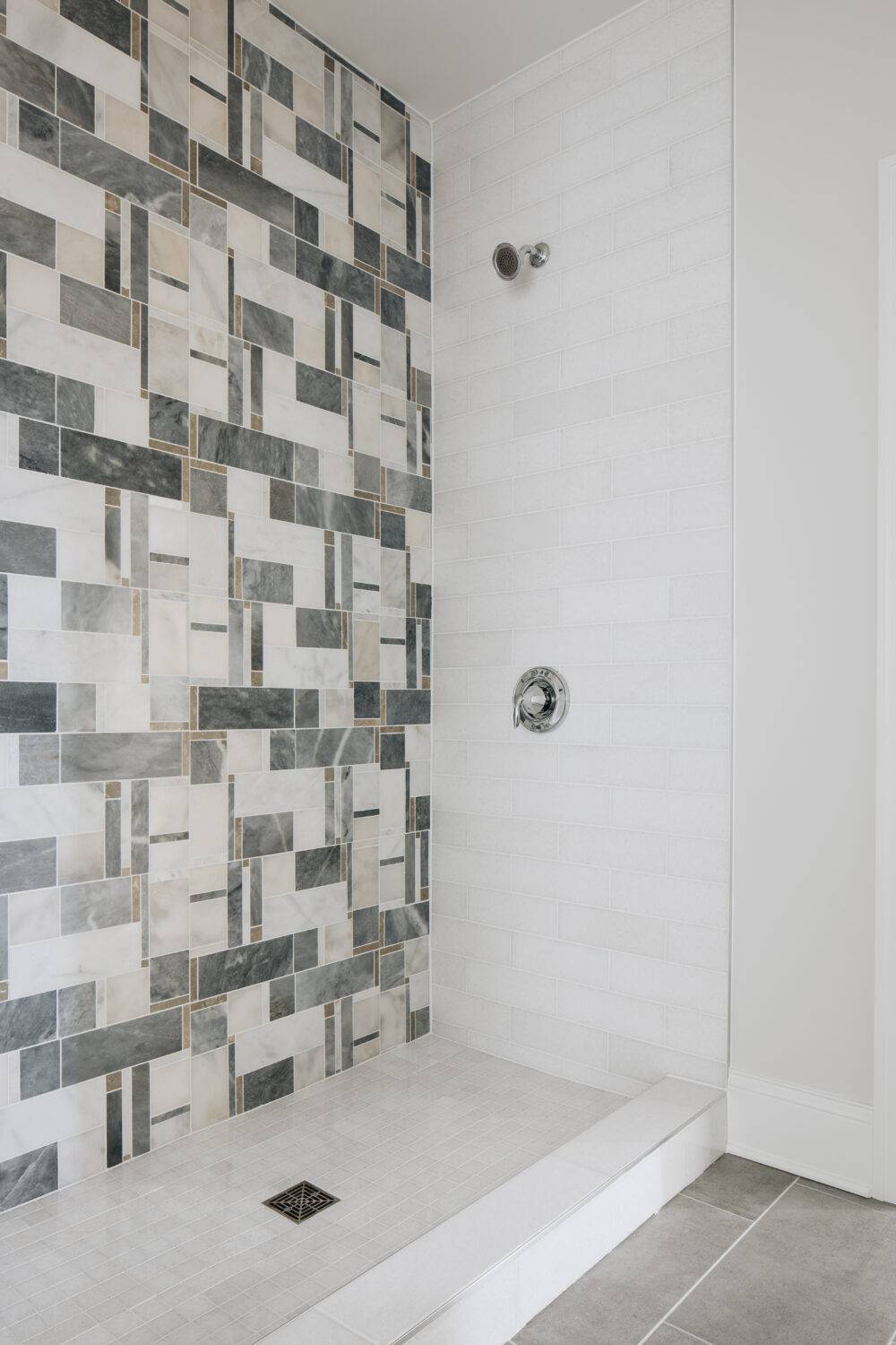 A modern shower with an intricate mosaic tile wall with grey white and beige marble and travertine.