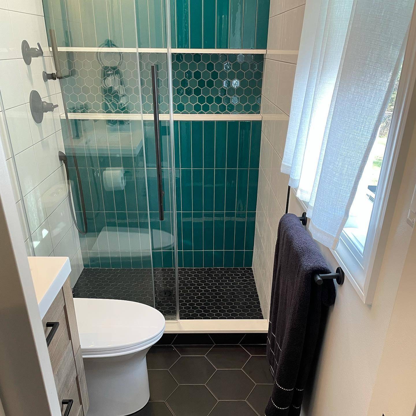 This vintage bathroom features teal subway tile and hexagon tile shower shelf and a black hexagon tile floor. 