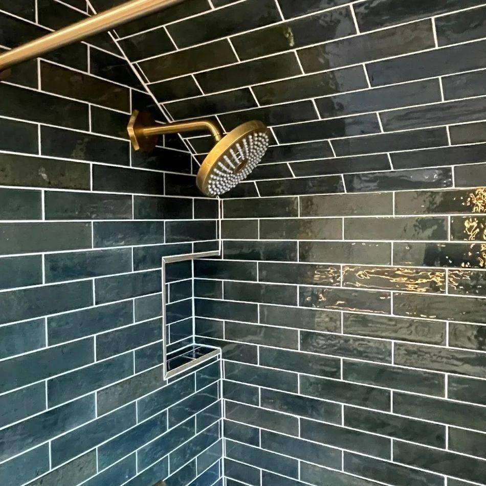 This shower features green handmade-look subway tile with white grout. 