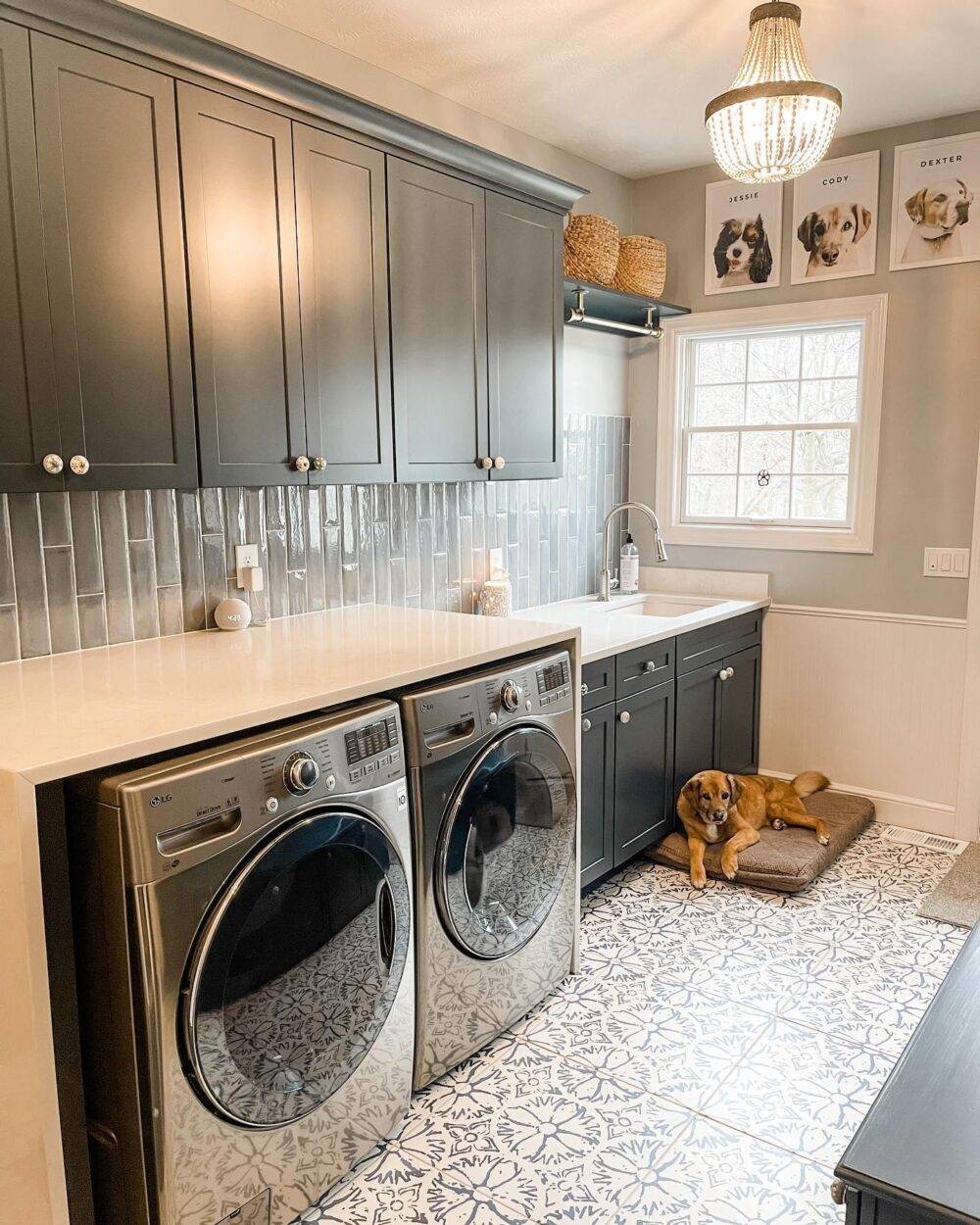 Laundry room featuring blue and white patterned tile floor, lounging upon which is a cute dog. 