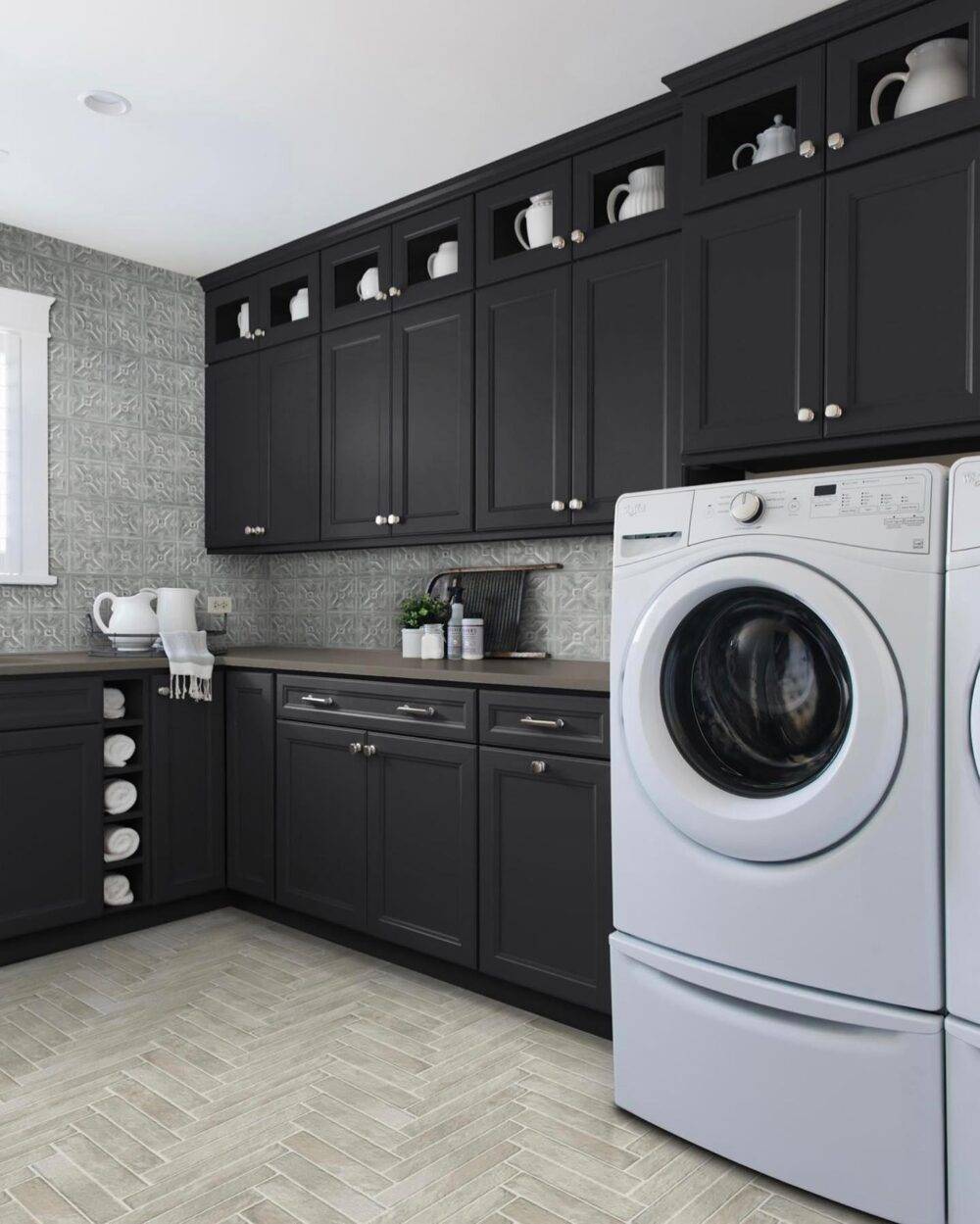 This laundry room features a greige patterned wall tile and brown herringbone tile floor. 