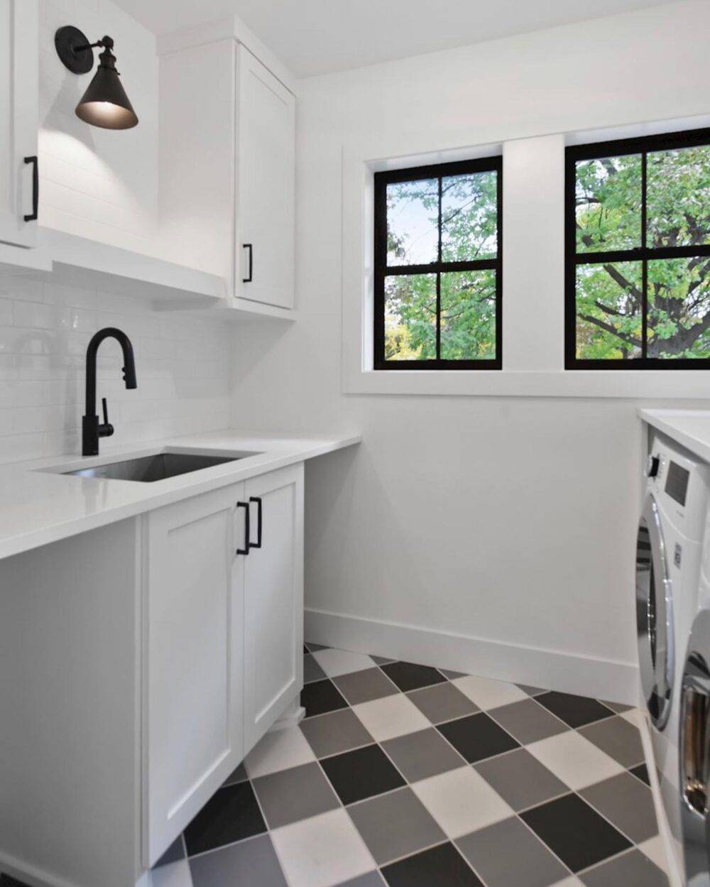 A bright white laundry room with black white and grey checkerboard tile floor.