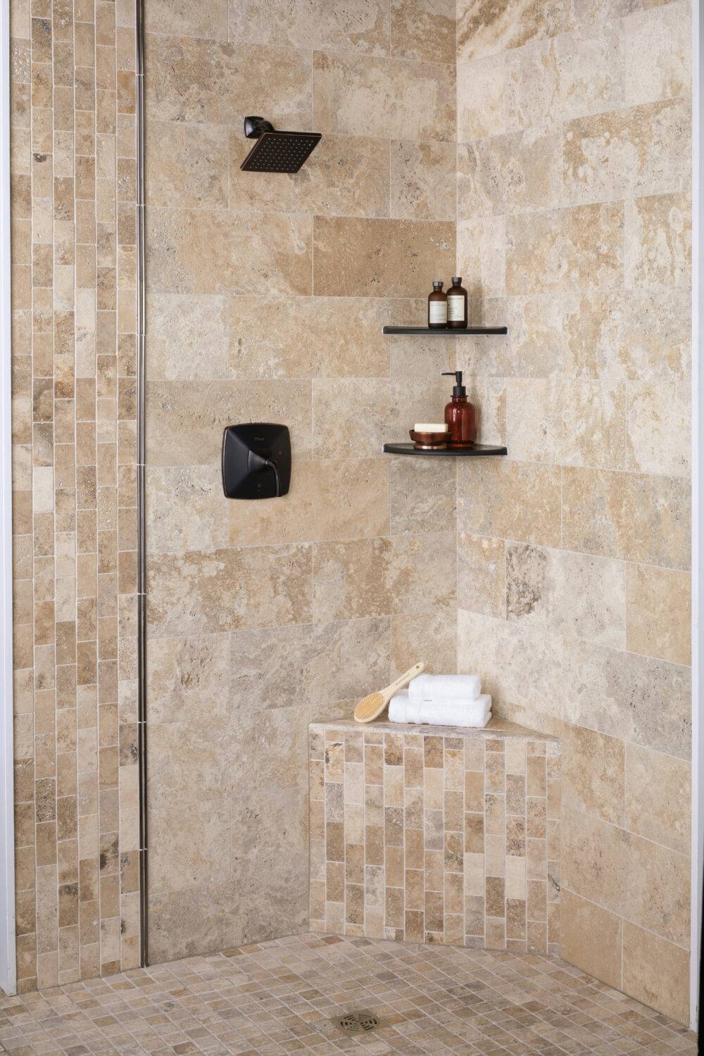 Walk In shower tiled in natural travertine stone with metallic profiles and corner shelves.