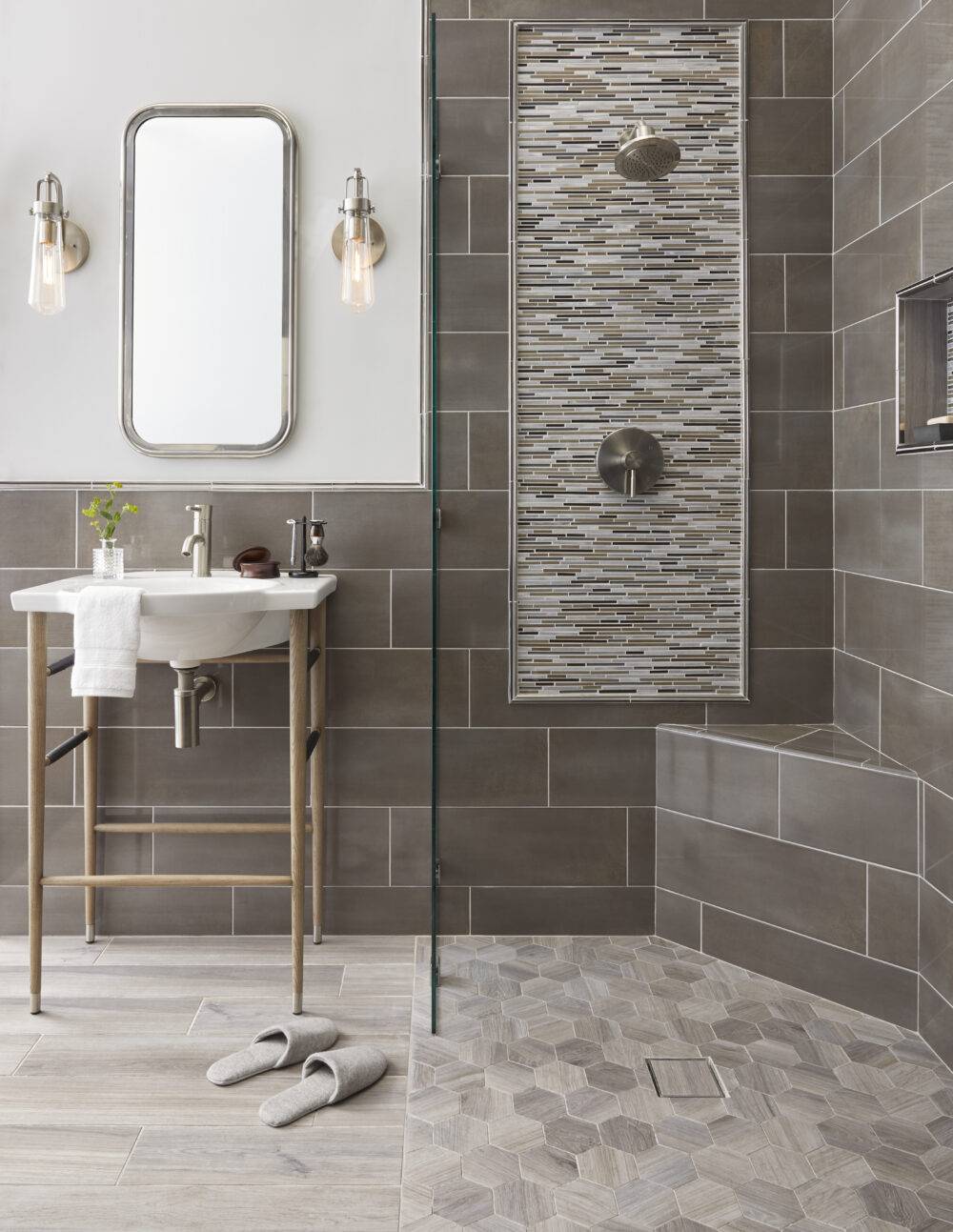 Bathroom tiled in warm tones.  Floor is wood look tile both rectangle and hexagonal shapes. Wall tile is horizontal staggered rectangles and deco frame is a metal and glass mosaic framed in metal pencil tiles.